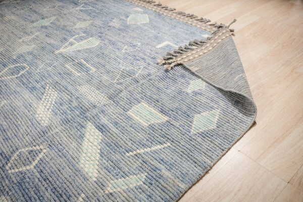A geometric blue, white, and mint low-pile rug with fringe detailing is visible on light wood plank flooring.