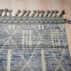 Textured blue and ivory rug with braided tassels rests on light wood plank flooring.