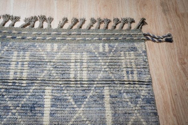 Textured blue and ivory rug with braided tassels rests on light wood plank flooring.