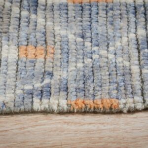 Chunky blue and cream high-pile rug with peach accents rests on a light wood grain floor.