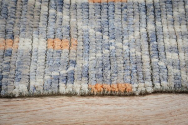 Chunky blue and cream high-pile rug with peach accents rests on a light wood grain floor.