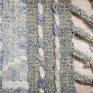 Detailed view of a striped blue and cream rug showing shaggy pile, flatweave, and thick heathered gray fringe.
