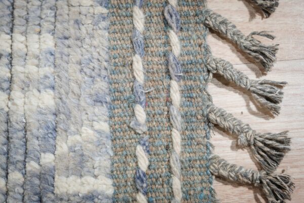 Detailed view of a striped blue and cream rug showing shaggy pile, flatweave, and thick heathered gray fringe.