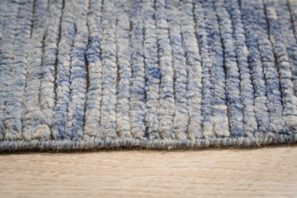 Close-up showing thick blue and tan variegated rug texture with vertical ridges on a light wood floor.