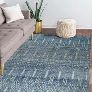 Blue geometric pattern rug with white and orange accents sits on a wood floor next to a gray sofa and braided pouf.