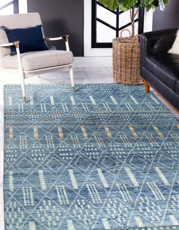 Blue geometric rug with white and orange accents covers tile floor near an armchair and black sofa.
