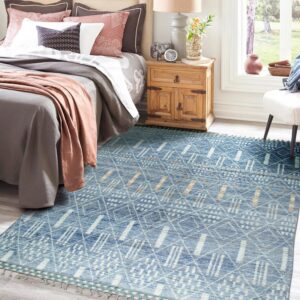 Blue geometric rug with white and tan patterns on gray plank flooring beside a wooden nightstand.