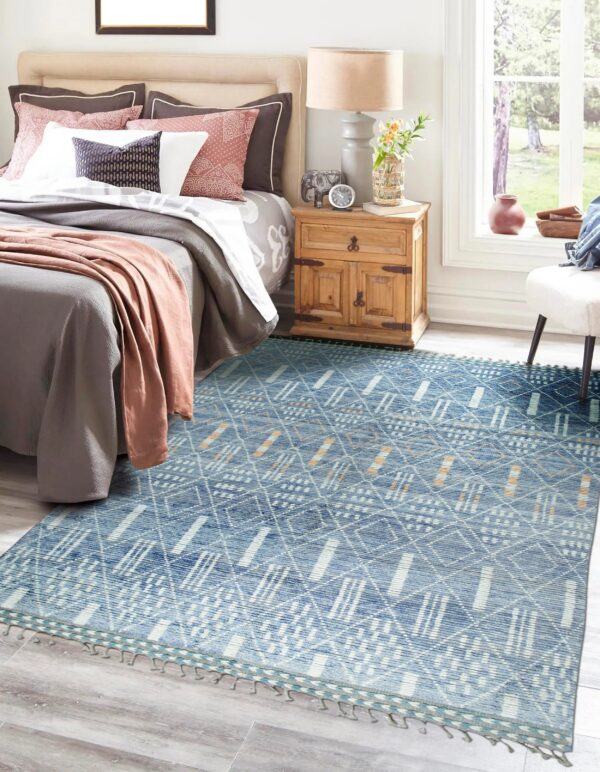Blue geometric rug with white and tan patterns on gray plank flooring beside a wooden nightstand.