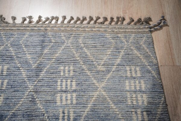 Textured blue and cream rug featuring a geometric pattern, thick fringe, and light wood flooring backdrop.