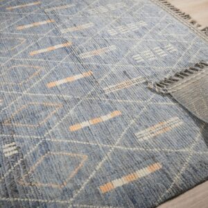 High-pile blue rug features white and peach geometric patterns; corner rolled back on light wood floor.