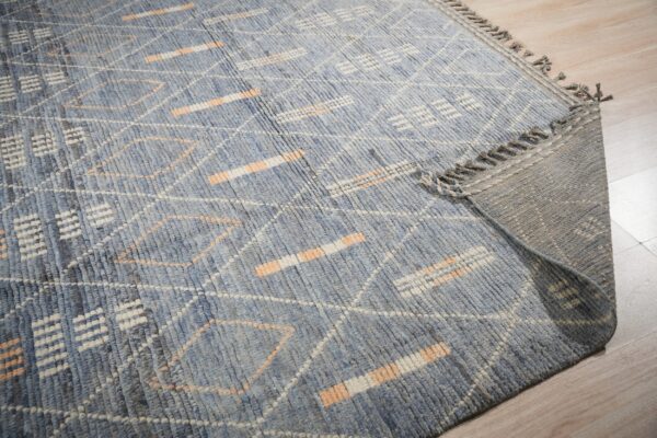 High-pile blue rug features white and peach geometric patterns; corner rolled back on light wood floor.
