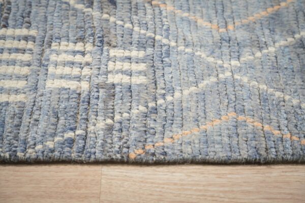 Chunky blue and cream high-pile rug with subtle peach diagonal accents rests on light wood flooring.