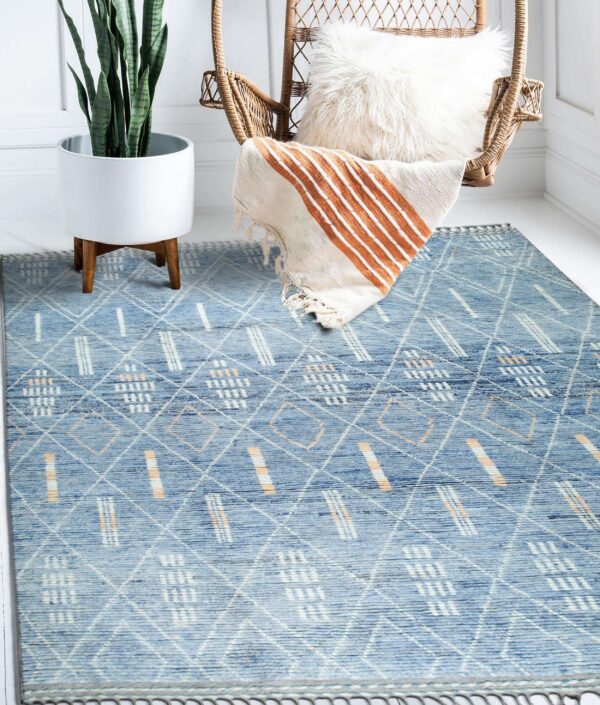 Blue rug with white and peach diamond and dash patterns anchors a bright corner with a potted plant and wicker chair.