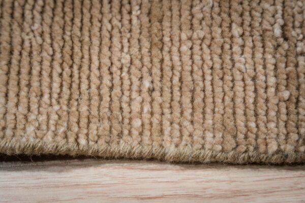A close view shows a thick, beige, ribbed rug pile resting on light wood flooring.