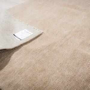 Light tan, high-pile rug with ribbed texture, partially rolled up on pale wood planks.