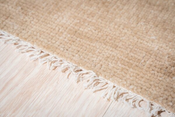 A light beige high-pile textured rug edge with white fringe lies on pale wood planks.