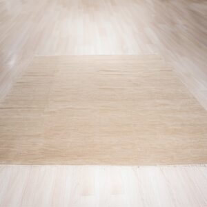 Beige rectangular rug with slight pile texture centered on light wood plank flooring.