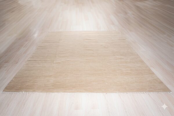 Beige rectangular rug with slight pile texture centered on light wood plank flooring.