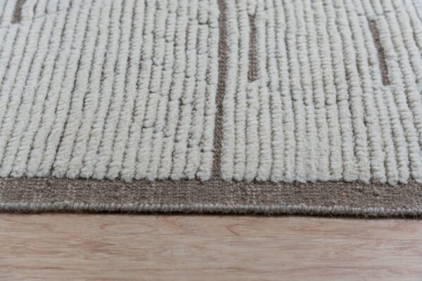 Chunky looped off-white rug with vertical brown patterns and a flat border on light wood flooring.
