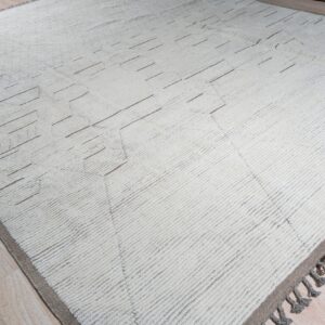 Shaggy cream rug with subtle taupe geometric lines and matching tassels on light wood planks.