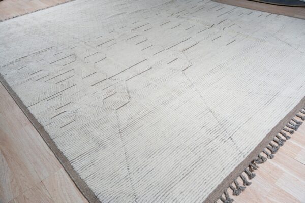 Shaggy cream rug with subtle taupe geometric lines and matching tassels on light wood planks.