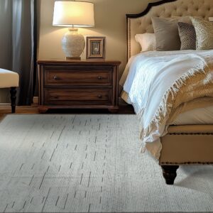 A ribbed gray rug with darker accent dashes sits on wood flooring beside a dark wood nightstand and upholstered bed.