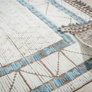 Textured white rug with blue and brown geometric accents is partially rolled back on light wood flooring.