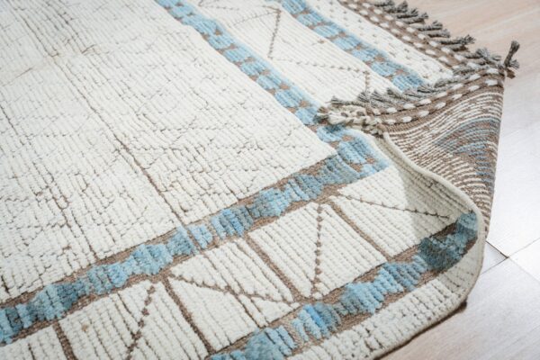 Textured white rug with blue and brown geometric accents is partially rolled back on light wood flooring.
