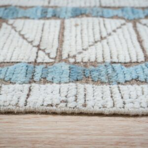 Cream and blue textured geometric rug edge resting on light blonde hardwood flooring.