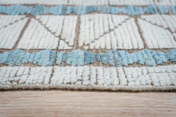 Cream and blue textured geometric rug edge resting on light blonde hardwood flooring.