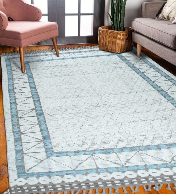 Light blue and gray geometric rug on wood floors between a pink armchair and a gray sofa.