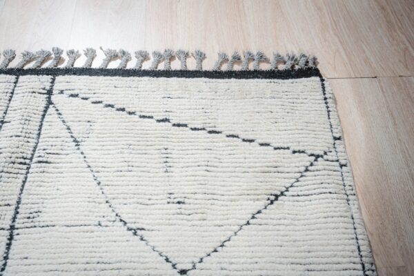 High-pile cream and dark gray rug with geometric lines and tassels rests on light wood plank flooring.