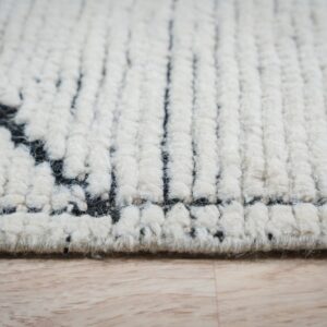 Cream high-pile rug detail showing black geometric patterns and thick texture resting on light wood.