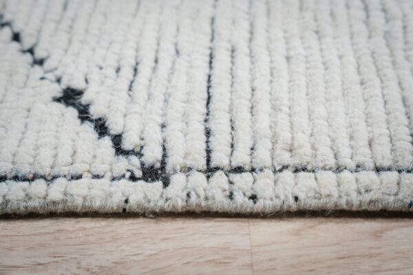 Cream high-pile rug detail showing black geometric patterns and thick texture resting on light wood.