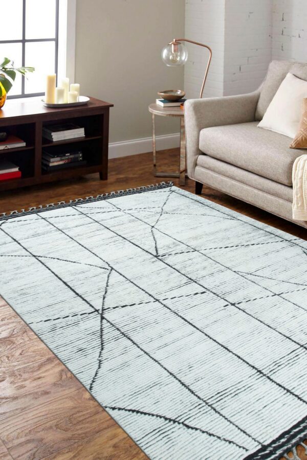 Textured white rug featuring a loose black grid design lies on wood flooring next to a gray sofa.