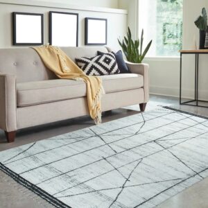 White textured rug with thin black geometric lines rests on a gray floor next to a beige sofa.