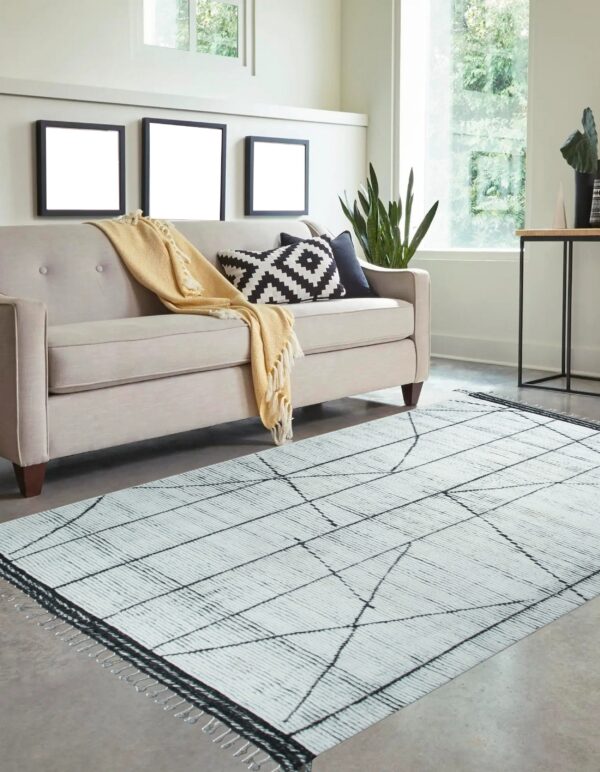 White textured rug with thin black geometric lines rests on a gray floor next to a beige sofa.