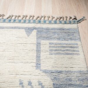 High-pile rug in cream and pale blue with tassels, featuring a geometric pattern on light wood planks.