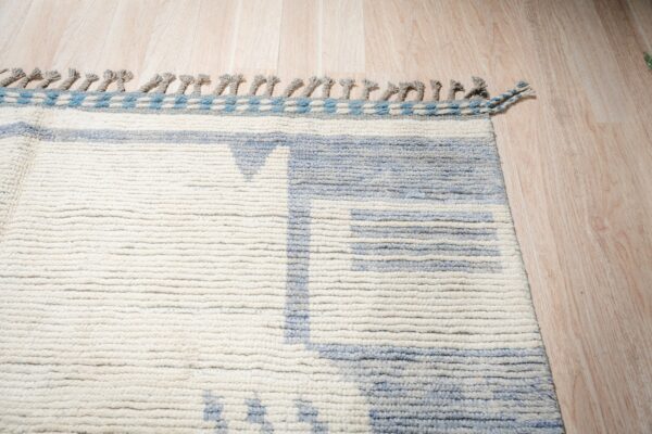 High-pile rug in cream and pale blue with tassels, featuring a geometric pattern on light wood planks.