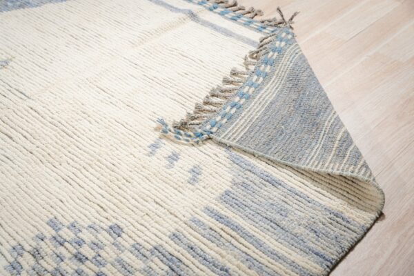 Thick cream and blue textured rug with fringe, partially folded over light wood flooring.