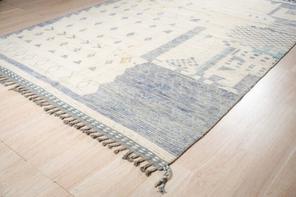 Textured cream and blue geometric rug with tassels displayed on light wood plank flooring.