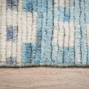 Chunky pile rug featuring an abstract pattern of cream, light blue, and gray fibers over wood grain.