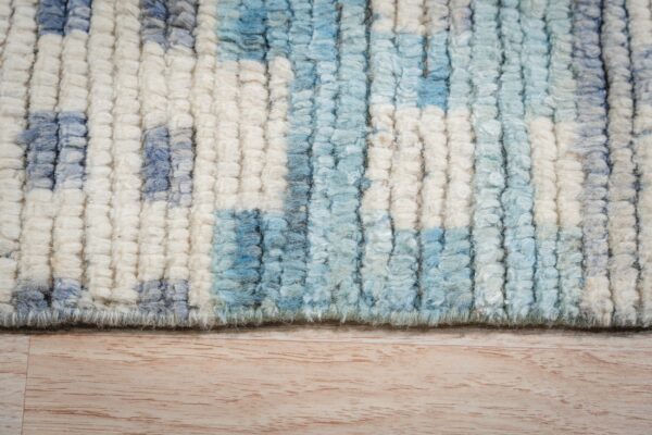 Chunky pile rug featuring an abstract pattern of cream, light blue, and gray fibers over wood grain.
