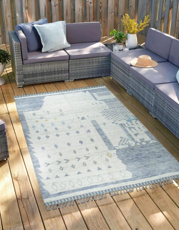 Geometric blue and white rug with tassels on a sunlit wooden deck, next to grey patio furniture.