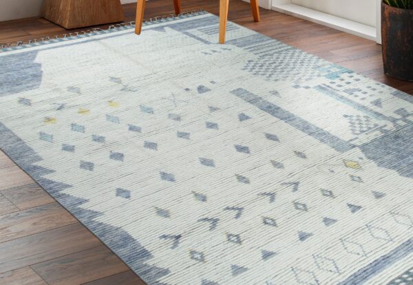 Off-white ribbed rug with blue geometric shapes and yellow accents lies on dark wood flooring.