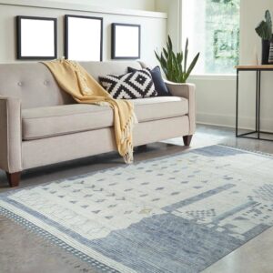 Abstract blue and white low-pile rug with fringe accents beneath a beige sofa on gray flooring.