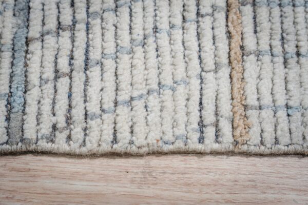 High-pile rug edge shows cream, blue, grey, and tan striped texture against light wooden flooring.