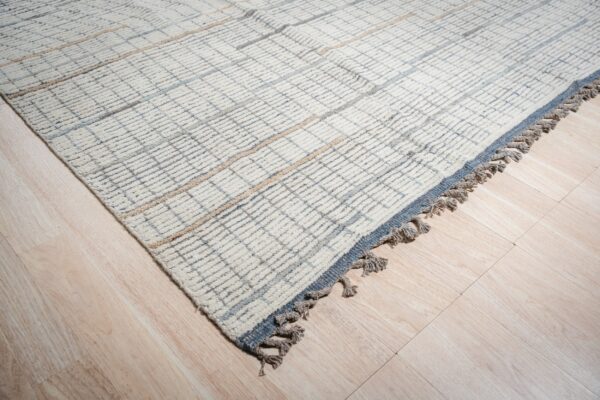 Close-up of a cream high-pile rug featuring a subtle blue and beige grid on light wood flooring.