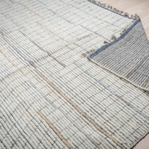 Close up of a cream rug with a looped grid pattern, revealing its striped grey and blue woven backing.
