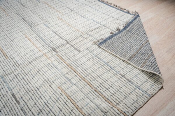 Close up of a cream rug with a looped grid pattern, revealing its striped grey and blue woven backing.